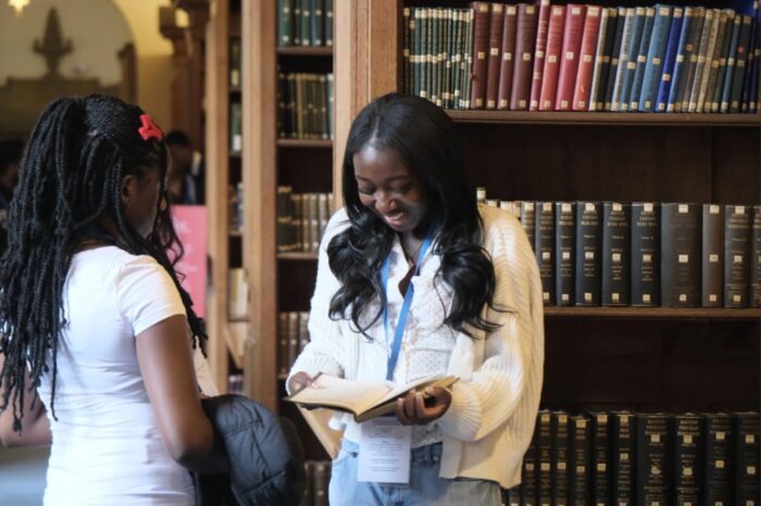You'll Fit In students at the Cambridge University Library, looking at a book in the collection.