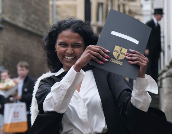 Colour photo of a student holding their diploma up whilst smiling at the camera.