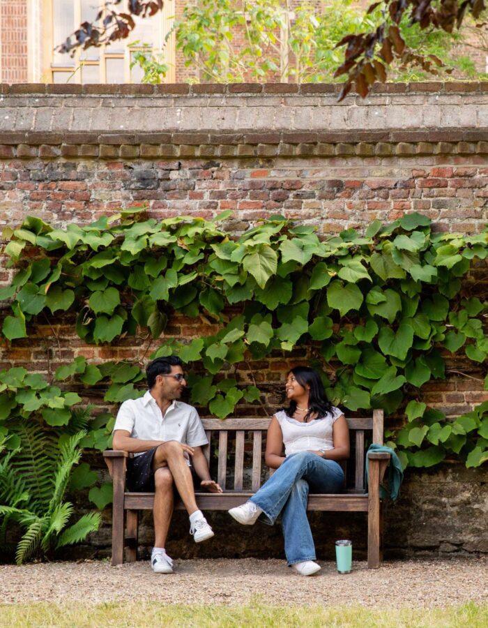 Colour photo of two students, one male and one female, having a conversation whilst sitting on a bench.