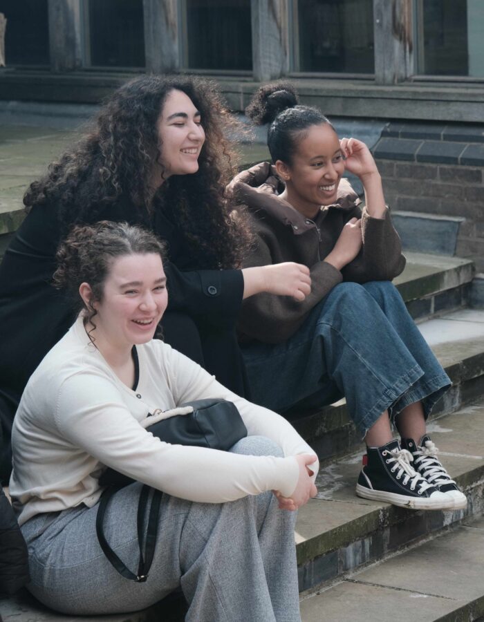 Colour image of three young women smiling whilst in conversation.